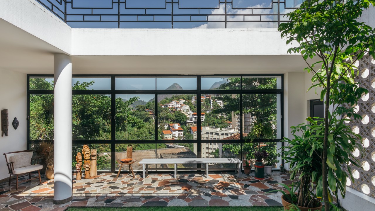 Casa de casal de 70 anos apaixonado por samba inspira-se na brasilidade. Projeto de Ana Cano. Na foto, área externa com piso de azulejo colorido e gramado.
