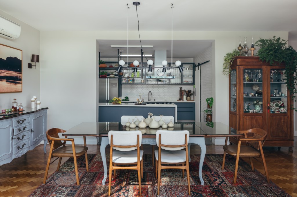 Casa de casal de 70 anos apaixonado por samba inspira-se na brasilidade. Projeto de Ana Cano. Na foto, sala de jantar vintage integrada com cozinha com marcenaria azul. Piso de taco.