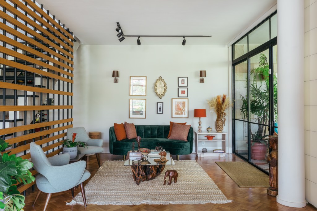 Casa de casal de 70 anos apaixonado por samba inspira-se na brasilidade. Projeto de Ana Cano. Na foto, sala com parede verde clara, sofá curvo verde e quadros.