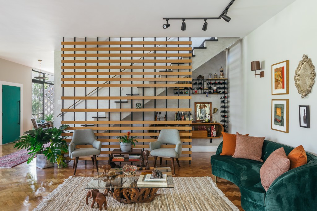 Casa de casal de 70 anos apaixonado por samba inspira-se na brasilidade. Projeto de Ana Cano. Na foto, sala de estar com elemento de madeira vazada na escada.