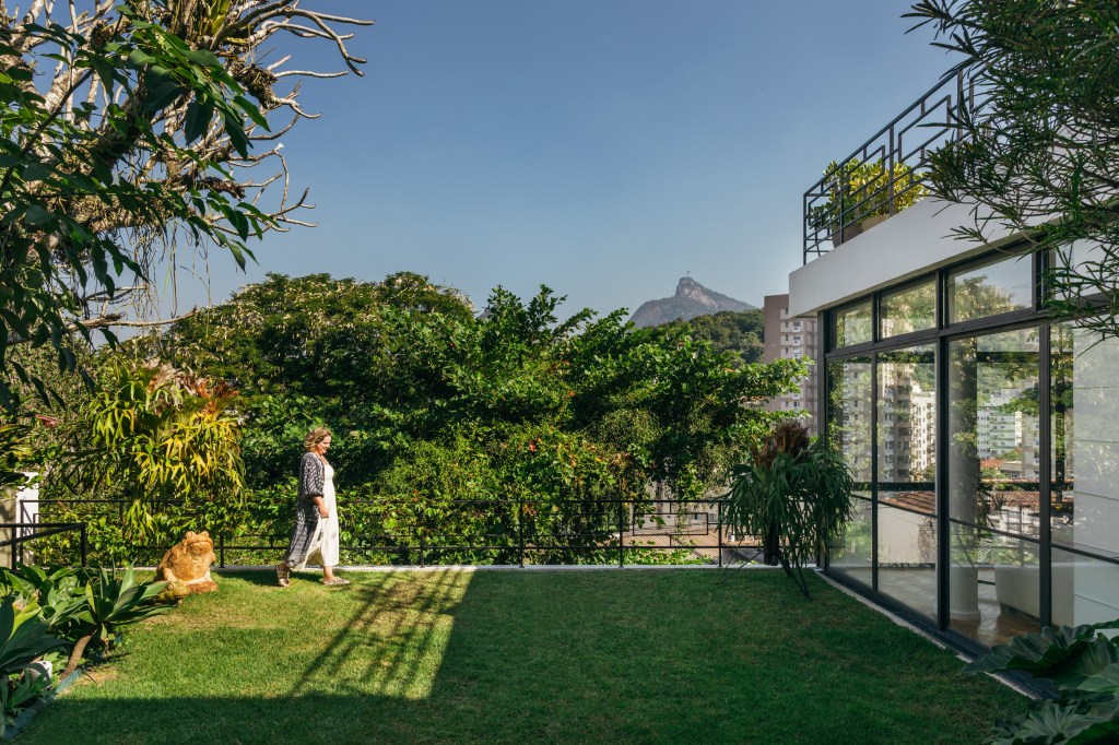 Casa de casal de 70 anos apaixonado por samba inspira-se na brasilidade. Projeto de Ana Cano. Na foto, jardim com gramado.