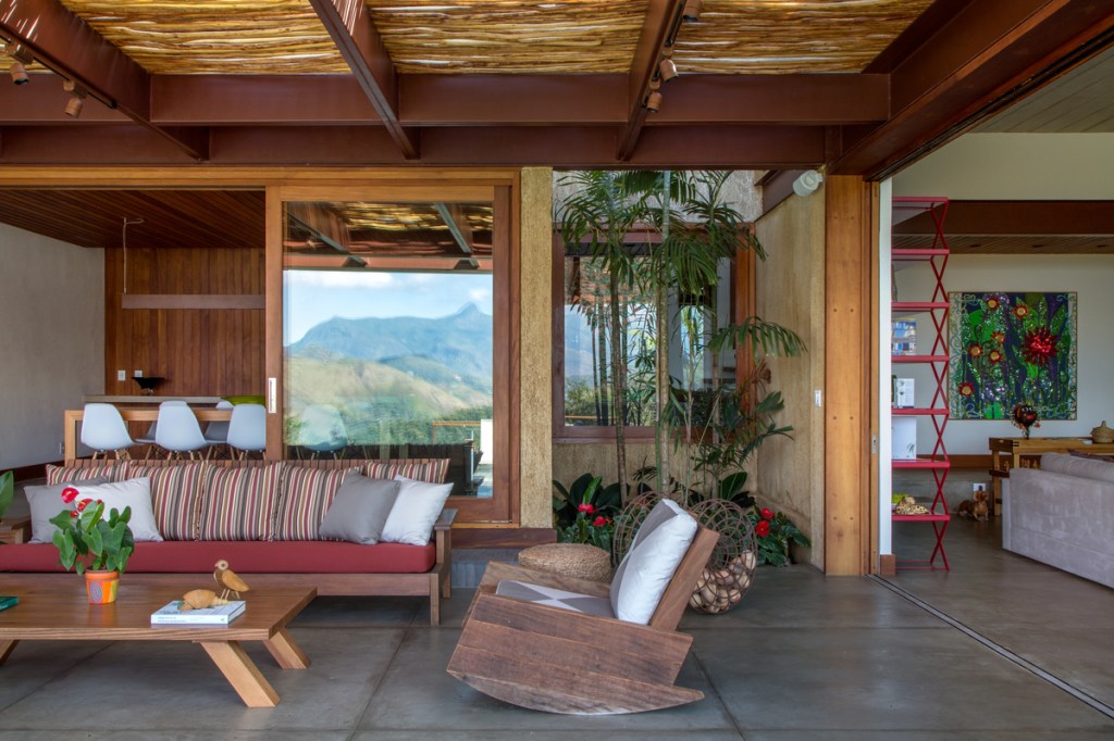 Casa na serra imersa na natureza possui vista espetacular para montanhas. Projeto de Andrea Chicharo. Na foto, varanda com vista para a Serra, sofá e plantas.
