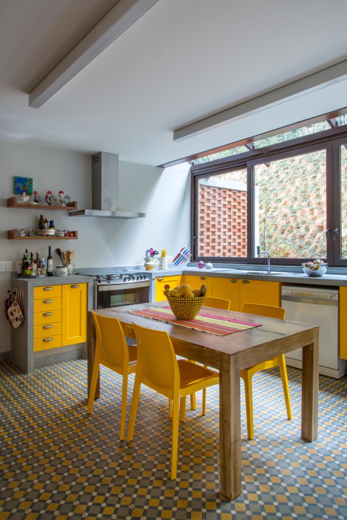 Casa na serra imersa na natureza possui vista espetacular para montanhas. Projeto de Andrea Chicharo. Na foto, cozinha com piso de ladrilho hidráulico e marcenaria amarela.