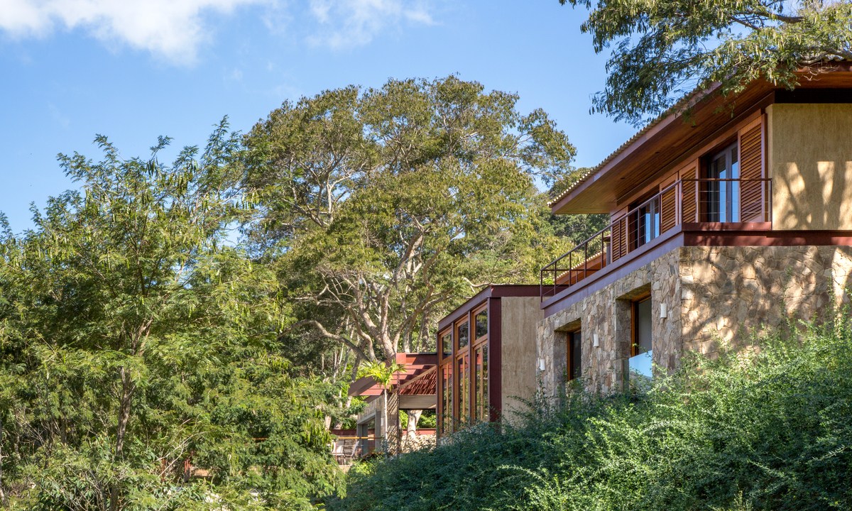 Casa na serra imersa na natureza possui vista espetacular para montanhas. Projeto de Andrea Chicharo. Na foto, fachada da casa com jardim e vista para a serra.