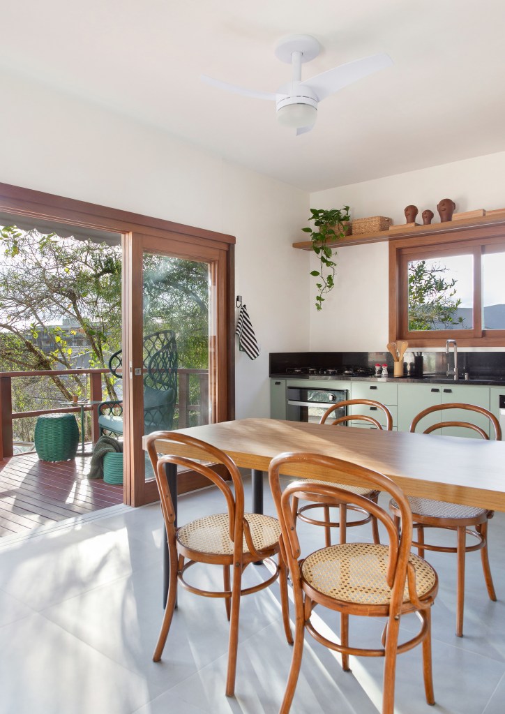 Cozinha de 15m² tem estilo contemporâneo com toque campestre. Projeto de Travessa Arquitetura. Na foto, cozinha com copa, bancada preta e armários verde claros. Porta para varanda.