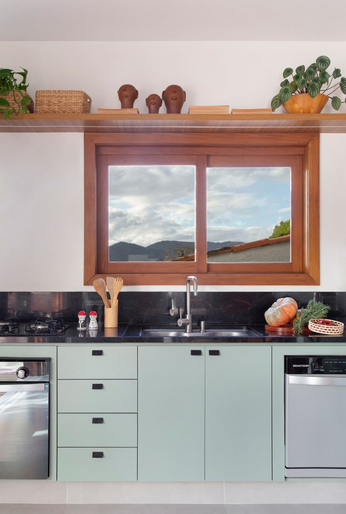 Cozinha de 15m² tem estilo contemporâneo com toque campestre. Projeto de Travessa Arquitetura. Na foto, cozinha com copa, bancada preta e armários verde claros.