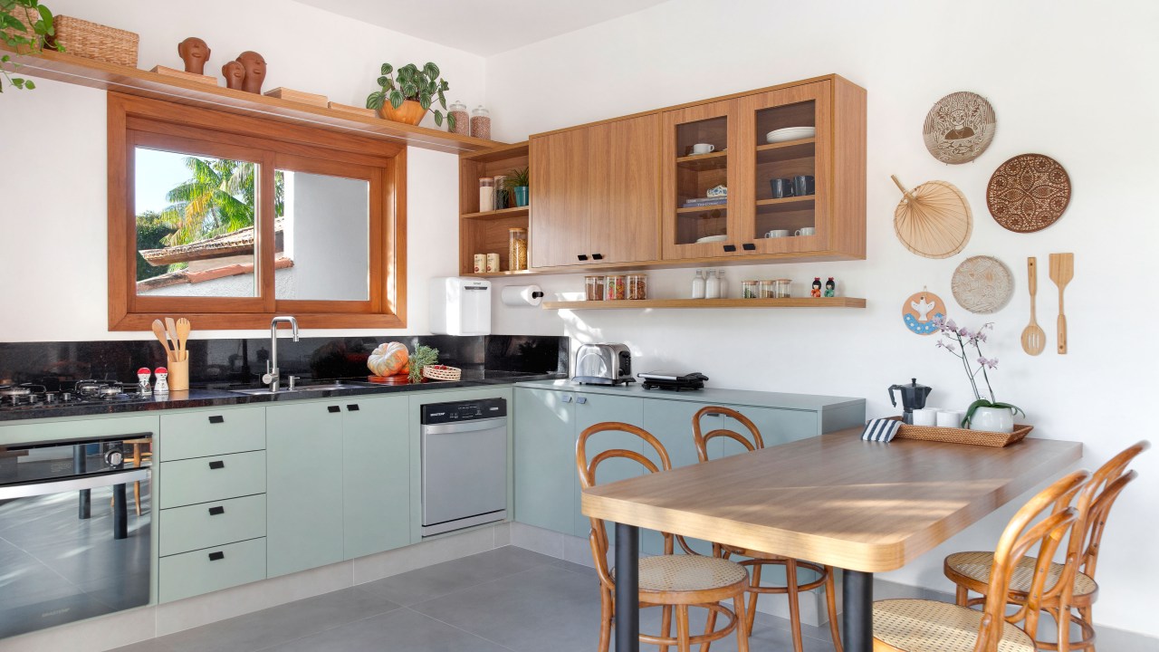 Cozinha de 15m² tem estilo contemporâneo com toque campestre. Projeto de Travessa Arquitetura. Na foto, cozinha com copa, bancada preta e armários verde claros.