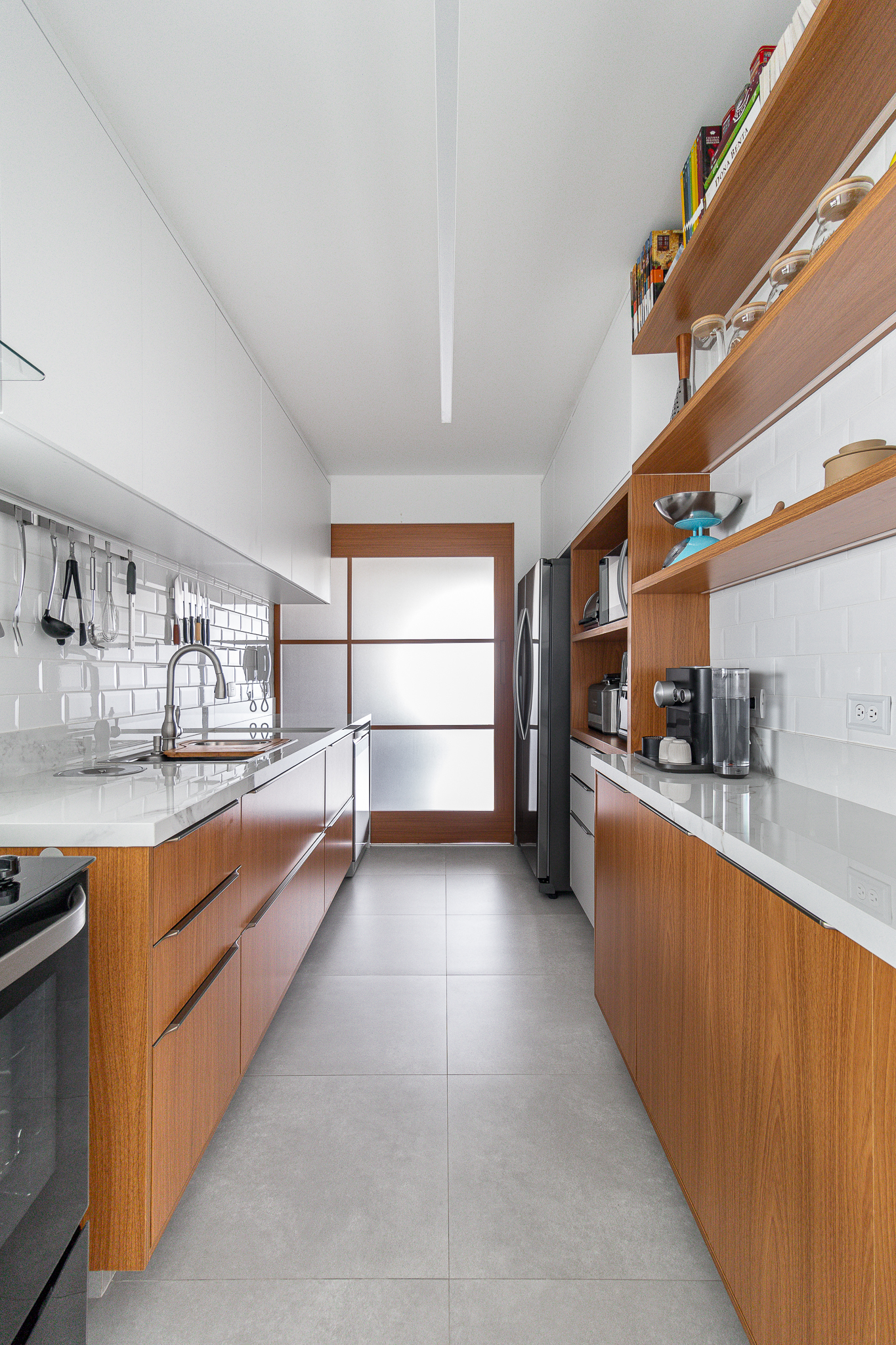 Cozinha minimalista foi pensada para abrigar muitos utensílios. Projeto de Inovando Arquitetura. Na foto, cozinha com piso de porcelanato, armários em madeira e bancada branca.
