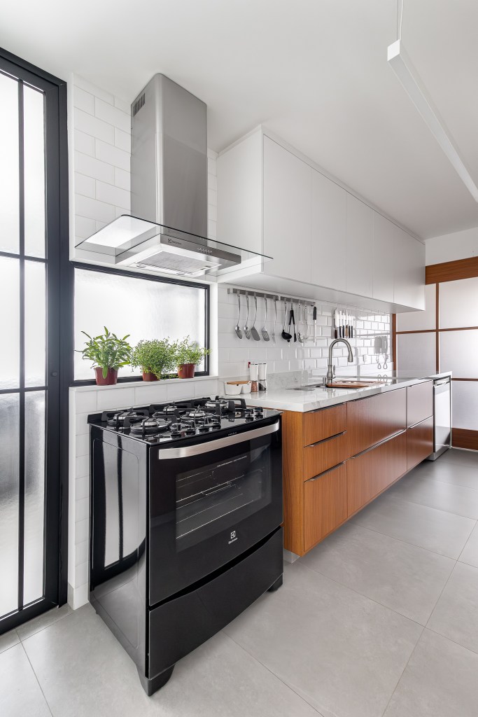 Cozinha minimalista foi pensada para abrigar muitos utensílios. Projeto de Inovando Arquitetura. Na foto, cozinha com porta de vidro para cozinha e armários brancos e madeira.