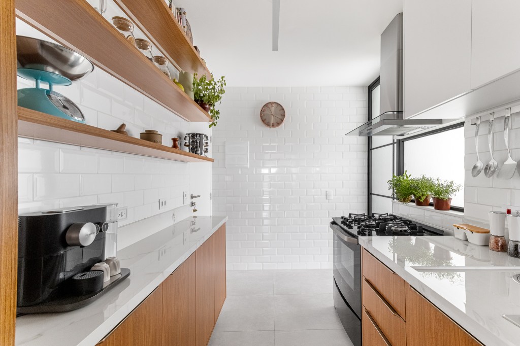 Cozinha minimalista foi pensada para abrigar muitos utensílios. Projeto de Inovando Arquitetura. Na foto, cozinha branca com bancada marmorizada.