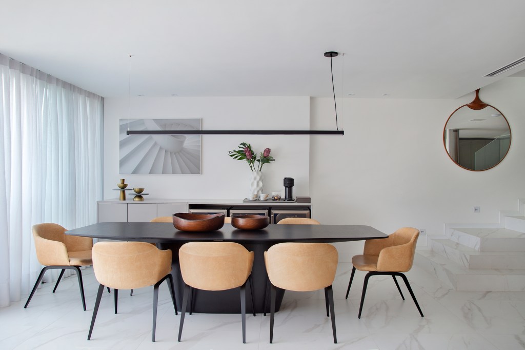 Duplex de 280 m² é minimalista, integrado e repleto de design brasileiro. Projeto de Tom Castro. Na foto, sala de jantar com mesa preta, cadeiras de couro e espelho.