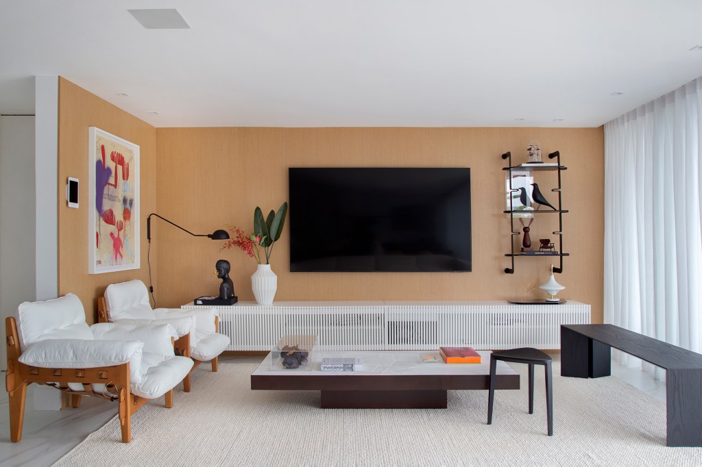 Duplex de 280 m² é minimalista, integrado e repleto de design brasileiro. Projeto de Tom Castro. Na foto, sala de tv com parede de madeira, aparador ripado e poltronas.
