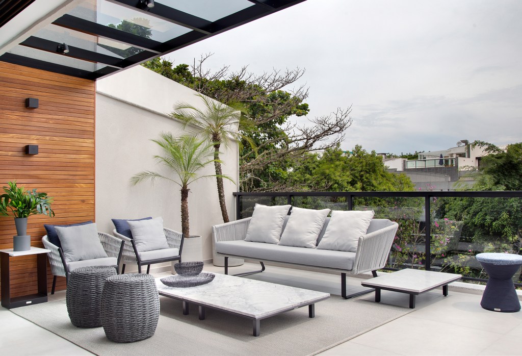 Duplex de 280 m² é minimalista, integrado e repleto de design brasileiro. Projeto de Tom Castro. Na foto, varanda com banco e vista para jardim, Pergolado de vidro.