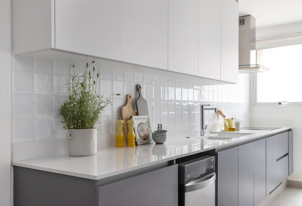 Janelas que trazem o verde para dentro e minimalismo definem apê de 170m². Projeto de AS Arquitetas. Na foto, cozinha minimalista branca com armários cinzas.