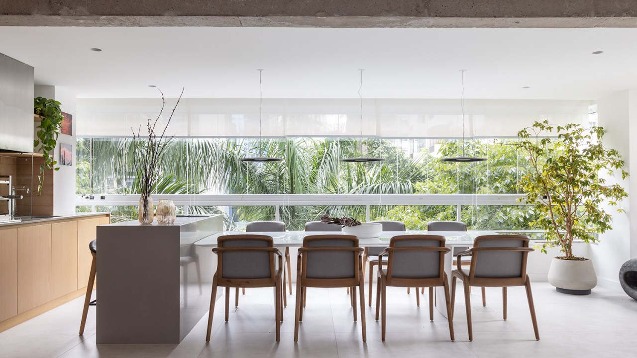 Janelas que trazem o verde para dentro e minimalismo definem apê de 170m². Projeto de AS Arquitetas. Na foto, sala integrada com varanda gourmet com mesa, bancada, churrasqueira e grandes janelas com vista para árvores.