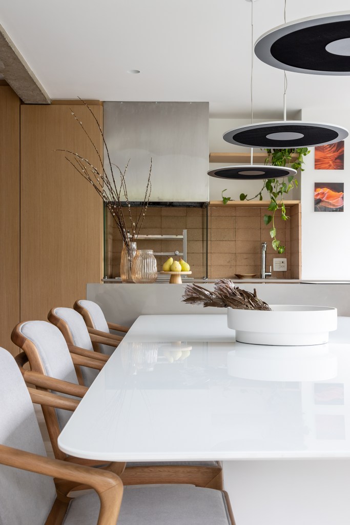 Janelas que trazem o verde para dentro e minimalismo definem apê de 170m². Projeto de AS Arquitetas. Na foto, varanda gourmet com bancada e mesa.