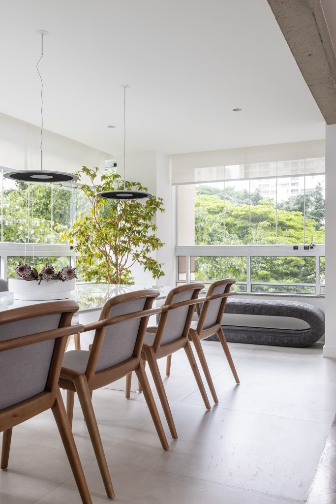 Janelas que trazem o verde para dentro e minimalismo definem apê de 170m². Projeto de AS Arquitetas. Na foto, varanda com grandes janelas e mesa de jantar. Área Gourmet.