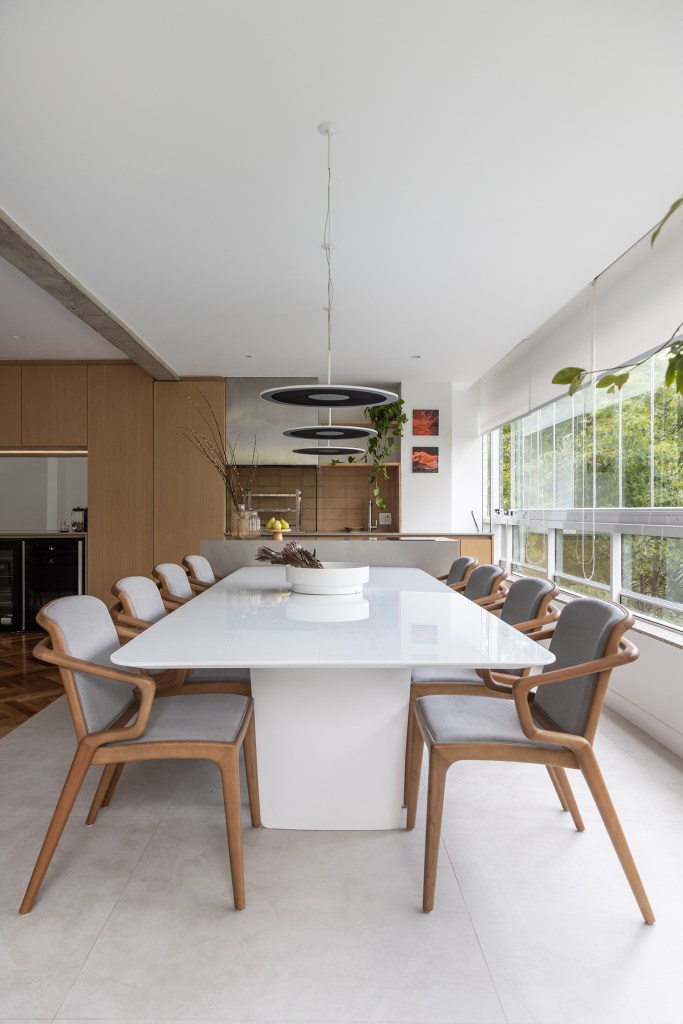 Janelas que trazem o verde para dentro e minimalismo definem apê de 170m². Projeto de AS Arquitetas. Na foto, varanda gourmet com bancada e mesa.