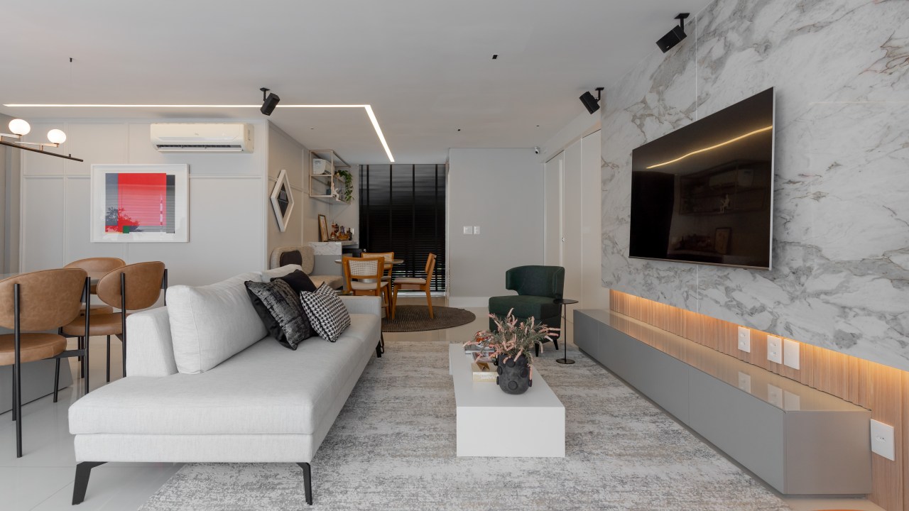 Móveis coloridos e mix de revestimentos dão o tom do décor neste apê. Projeto de Romário Rodrigues. Na foto, sala com tv, parede marmorizada e sofá branco.