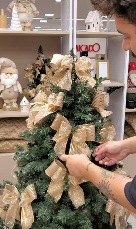 Passo a passo para montar uma Árvore de Natal igual às do shopping. Na foto, laço sendo colocado na árvore.