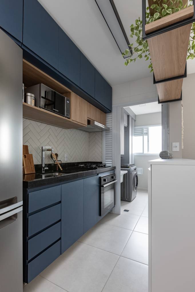 Sem quebra-quebra, apê de 53 m² ganha cores e canto alemão com sapateira. Projeto de Studio Monfré. Na foto, cozinha integrada com marcenaria azul e backsplash chanfrado.