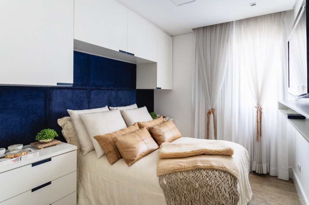 Tons neutros e cimento queimado permeiam apê prático de 75m². Projeto de Erti Arquitetos. Na foto, quarto com armários em volta da cama brancos e parede azul marinho.