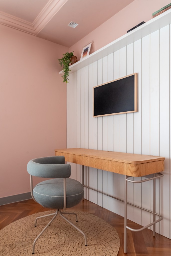 Ambientes Peach Fuzz. Projeto de Mari Milani. Na foto, home office no quarto com bancada de madeira e parede na cor peach fuzz. Parede com revestimento de lambri branco.