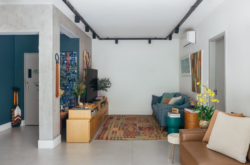 Apartamento de 140 m² parece uma casa em meio às árvores. Projeto Ana Cano. Na foto, sala de estar com tv, trilhos e tapete.
