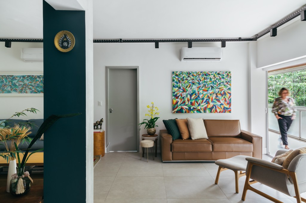 Apartamento de 140 m² parece uma casa em meio às árvores. Projeto Ana Cano. Na foto, sala de estar com sofá de couro e quadro;
