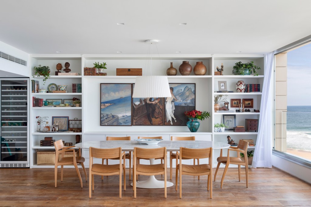 Apê de 250m² tem cozinha com três cubas e balcão de mármore verde. Projeto de Escala Arquitetura. Na foto, sala de jantar com cadeiras de madeira e estante branca.