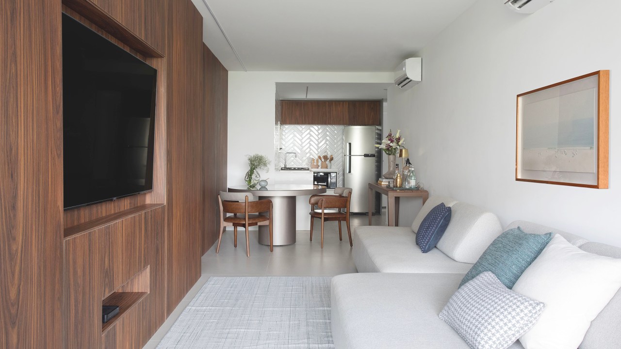 Apê de 75m² recebe décor minimalista em reforma de apenas 3 meses. Projeto de Roby Macedo. Na foto, sala de estar integrada com jantar e cozinha. Parede revestida de madeira escura.