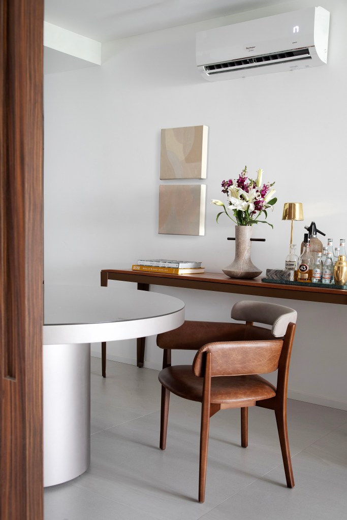 Apê de 75m² recebe décor minimalista em reforma de apenas 3 meses. Projeto de Roby Macedo. Na foto, sala de jantar com mesa redonda, duas cadeiras e aparador com bandeja de bebidas.