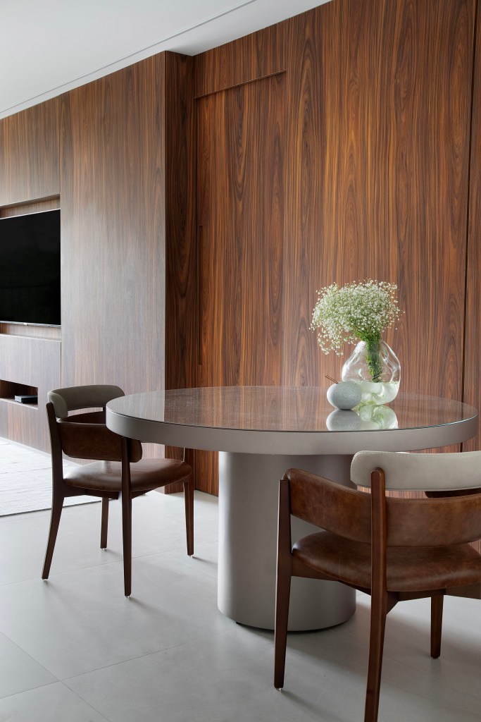 Apê de 75m² recebe décor minimalista em reforma de apenas 3 meses. Projeto de Roby Macedo. Na foto, sala de jantar com mesa redonda e parede revestida de madeira escura.