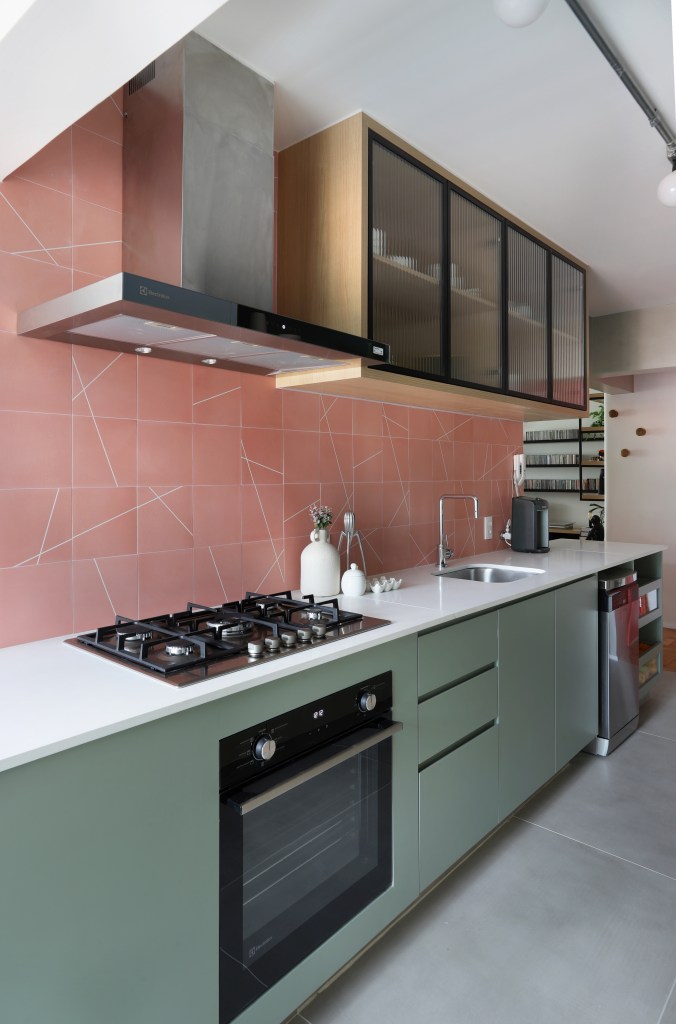 Apê de 90m² tem cozinha rosa, armário vermelho e guarda-roupa azul. Projeto de Studio 92 Arquitetura. Na foto, cozinha com backsplash de azulejos rosa e marcenaria verde.