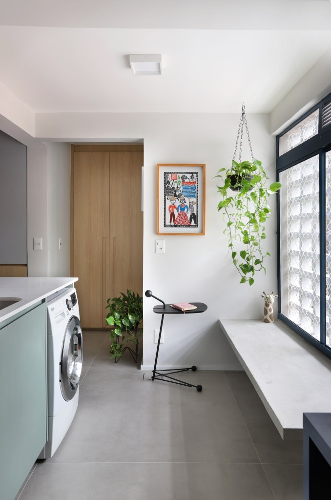 Apê de 90m² tem cozinha rosa, armário vermelho e guarda-roupa azul. Projeto de Studio 92 Arquitetura. Na foto, lavanderia com banco de cimento e planta suspensa.