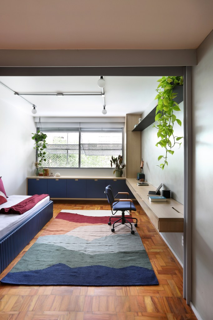 Apê de 90m² tem cozinha rosa, armário vermelho e guarda-roupa azul. Projeto de Studio 92 Arquitetura. Na foto, quarto de hóspedes com home office e bicama.