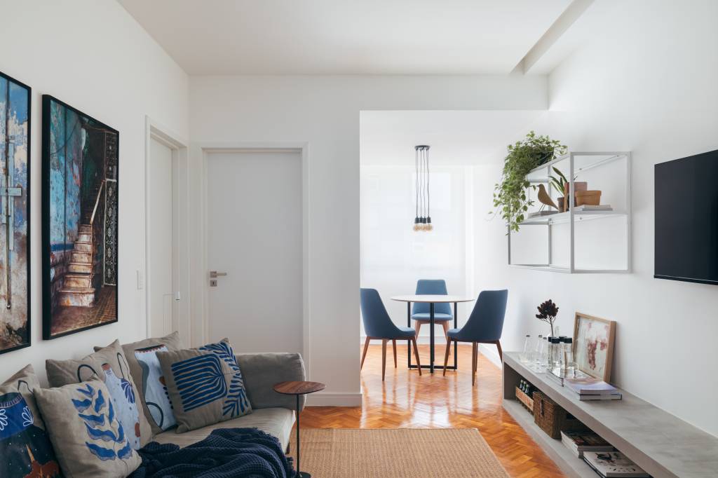 Apê de 90m² tem décor nórdico, com paredes brancas e armário aberto. Projeto de Bianca Da Hora. Na foto, sala de estar com piso de madeira, rack baixo, sofá cinza e sala de jantar ao fundo.