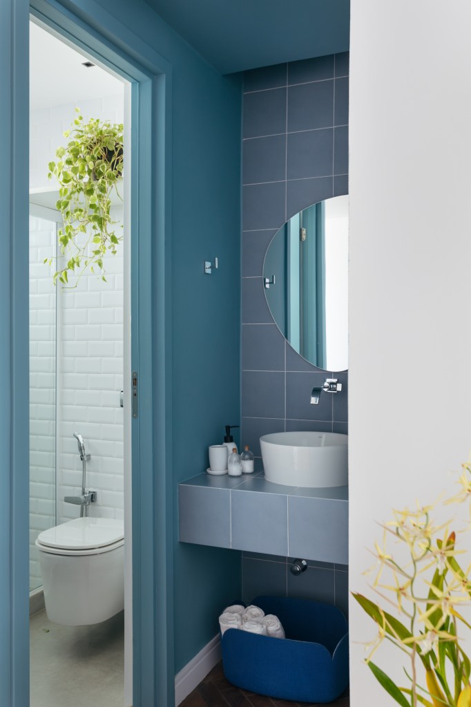 Apê de 90m² tem décor nórdico, com paredes brancas e armário aberto. Projeto de Bianca Da Hora. Na foto, lavabo azul com azulejos, cuba solta e espelho em formato orgânico. Plantas no banheiro.
