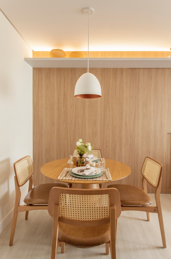 Apê compacto de 63m² usa móveis enxutos para aproveitar o espaço. Projeto de Carina Dal Fabbro. Na foto, sala de jantar pequena com mesa redonda e paredes revestidas com painel de madeira.