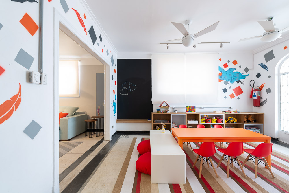 Áreas de lazer: confira 5 tipos de espaços para incluir no projeto. Projeto de Dantas & Passos Arquitetura. Na foto, brinquedoteca com mesa colorida laranja e tapete listrado.