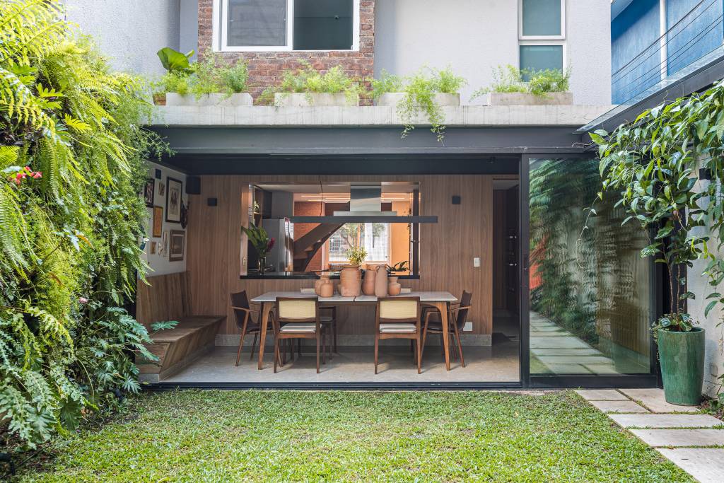 Casa de vila tem jardim com rede, cozinha integrada e muito charme. Projeto de Marcela Fazio Arquitetura. Na foto, área externa da casa com jardim e rede.