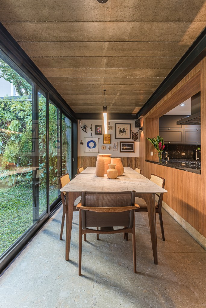 Casa de vila tem jardim com rede, cozinha integrada e muito charme. Projeto de Marcela Fazio Arquitetura. Na foto, sala de jantar integrada com cozinha, grandes portas de vidro para jardim.