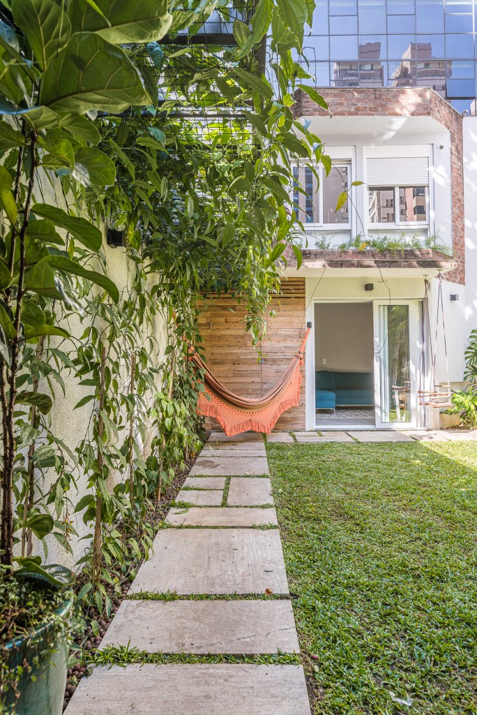 Casa de vila tem jardim com rede, cozinha integrada e muito charme. Projeto de Marcela Fazio Arquitetura. Na foto, área externa da casa com jardim e rede.