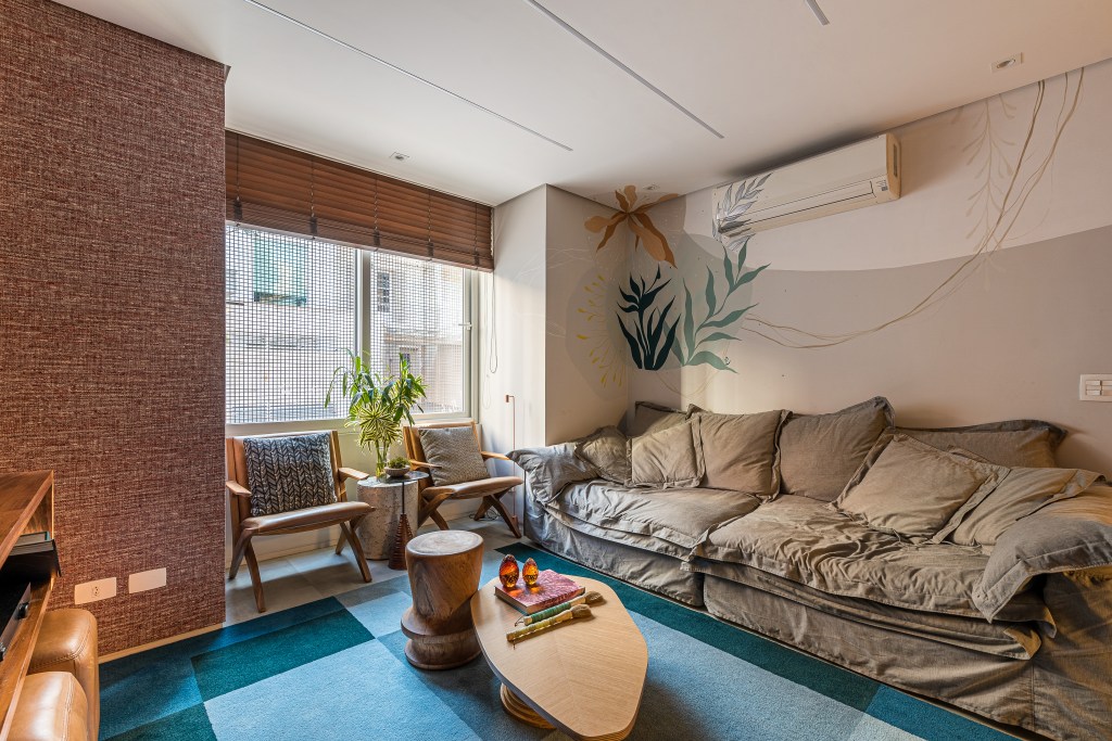 Casa de vila tem jardim com rede, cozinha integrada e muito charme. Projeto de Marcela Fazio Arquitetura. Na foto, sala de estar com sofá cinza, poltronas abaixo de janela e tapete azul.