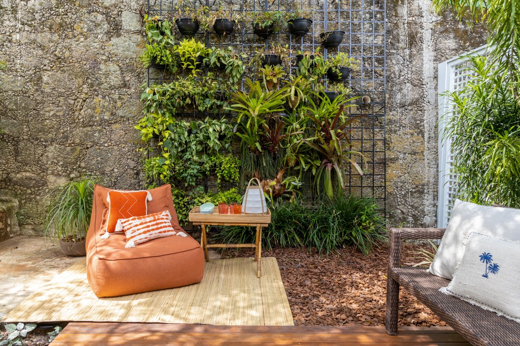 Cobertura carioca une charme, cores, plantas e espaços de convivência. Projeto de Hanna Lerner Arquitetura. Na foto, varanda com jardim vertical, poltrona e pedras.