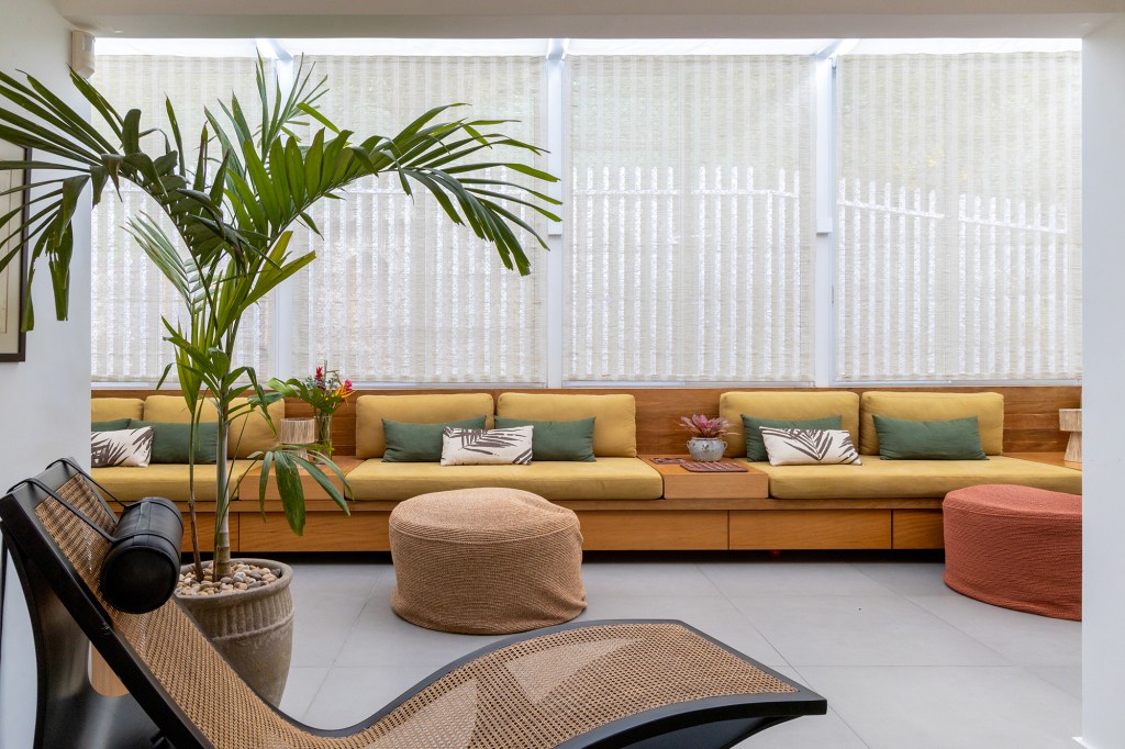 Cobertura carioca une charme, cores, plantas e espaços de convivência. Projeto de Hanna Lerner Arquitetura. Na foto, varanda com banco, sofá, mesas e plantas.