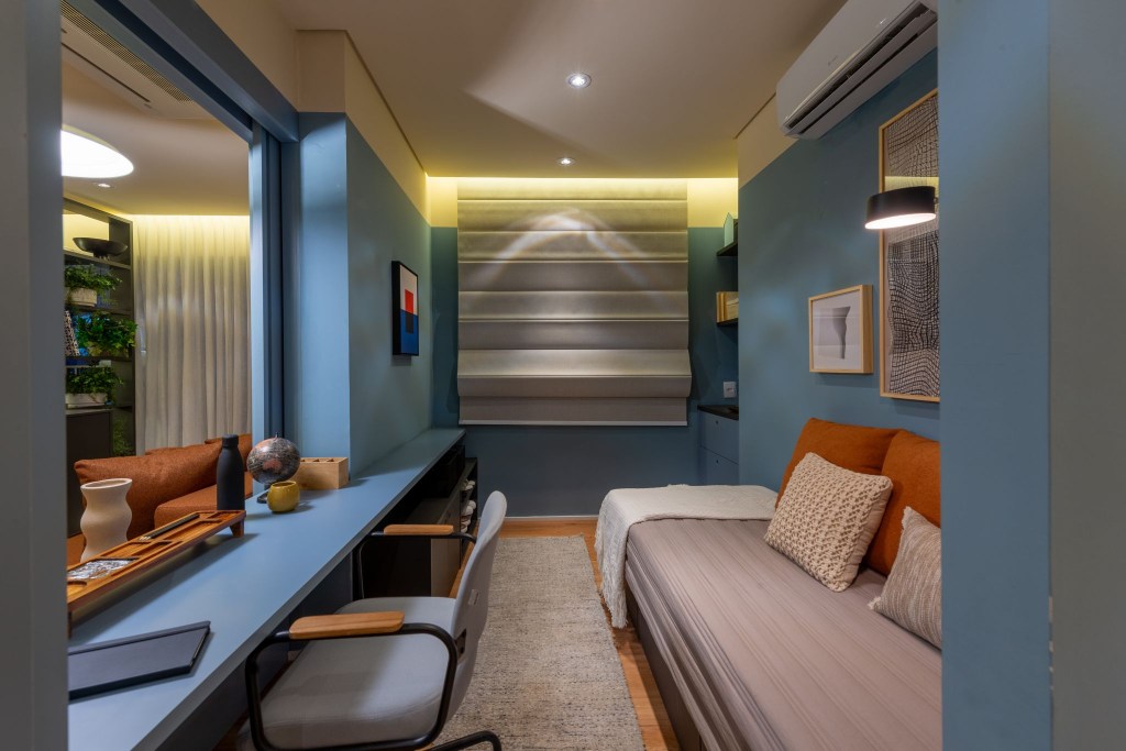 Cores vivas marcam apês de 64 e 85 m² assinados por Todos Arquitetura. Na foto, escritório com cama, parede azul e quadros.