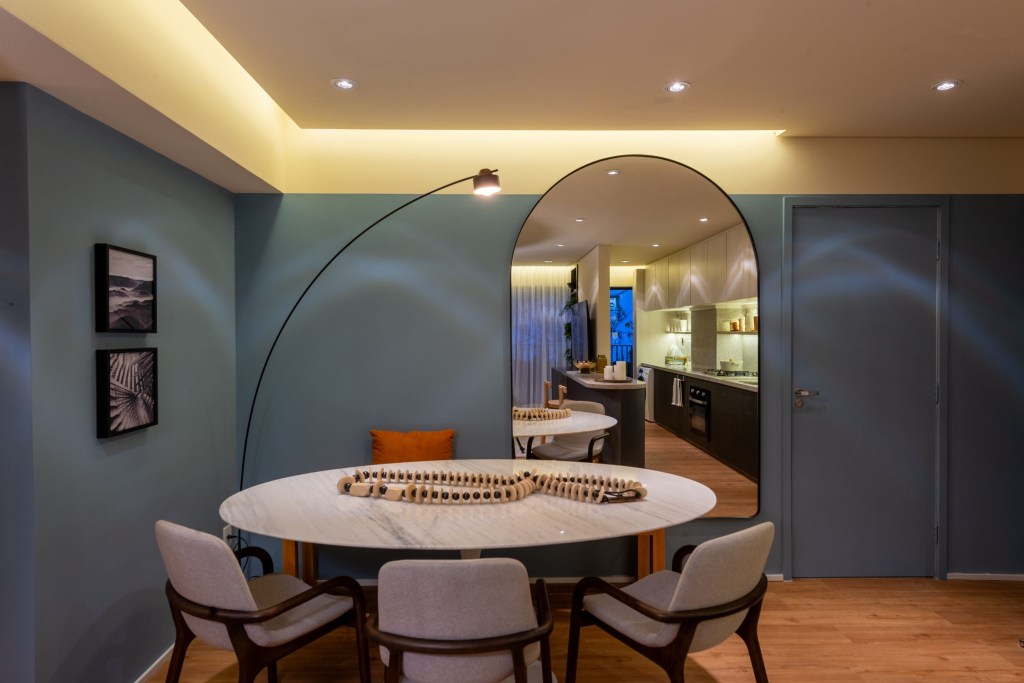Cores vivas marcam apês de 64 e 85 m² assinados por Todos Arquitetura. Na foto, sala de jantar com espelho, mesa redonda e paredes azuis.