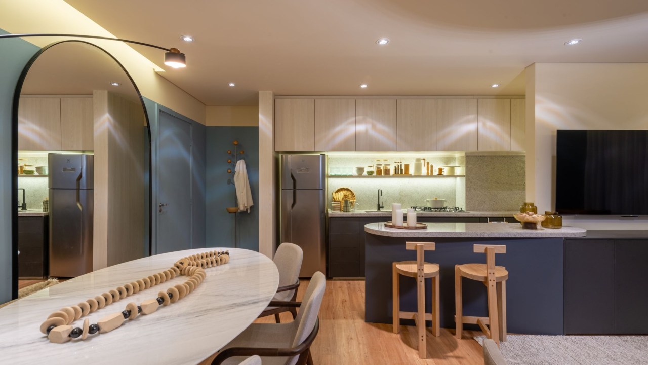 Cores vivas marcam apês de 64 e 85 m² assinados por Todos Arquitetura. Na foto, sala de jantar com espelho, mesa redonda e paredes azuis. Cozinha integrada com balcão.
