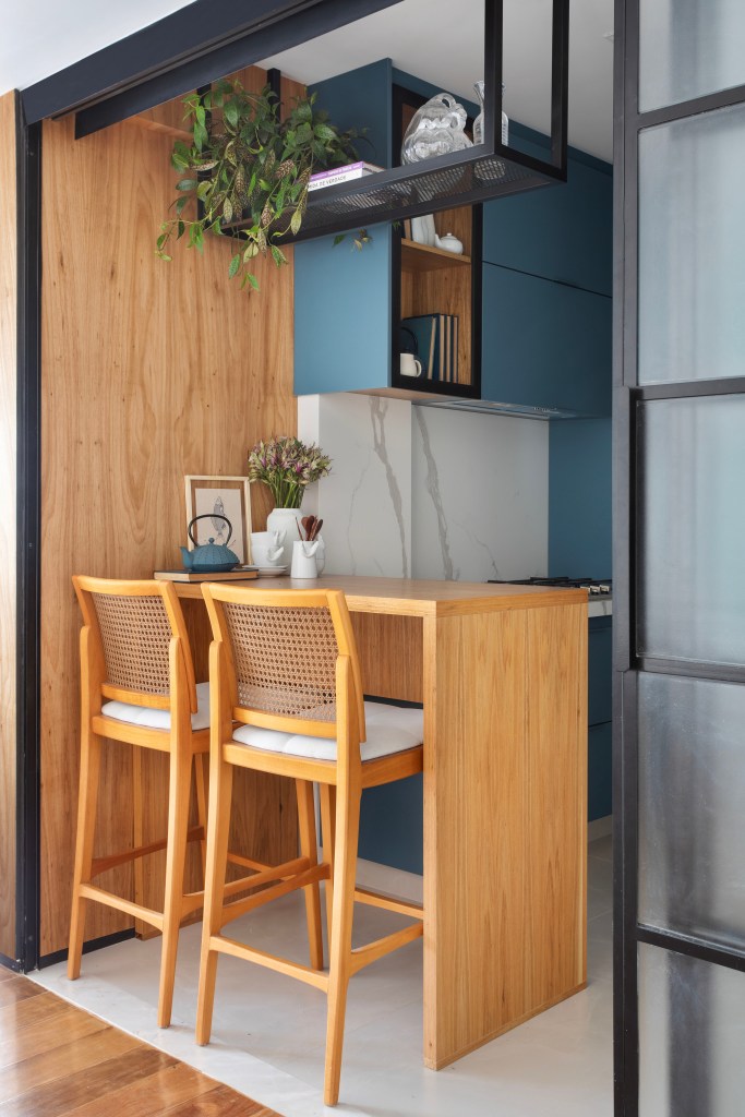 Estante com 50 nichos rouba a cena em sala de estar de apê de 150m². Projeto de Henrique Ramalho. Na foto, cozinha pequena com bancada pequena de madeira e marcenaria azul.